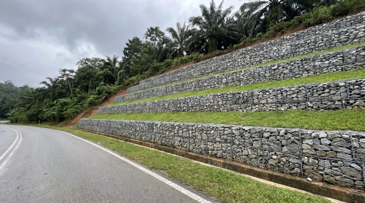 Cerun tepi jalan yang sama selepas diperkukuh dengan gabion bertingkat, setiap tingkat dipisahkan oleh teres berumput.