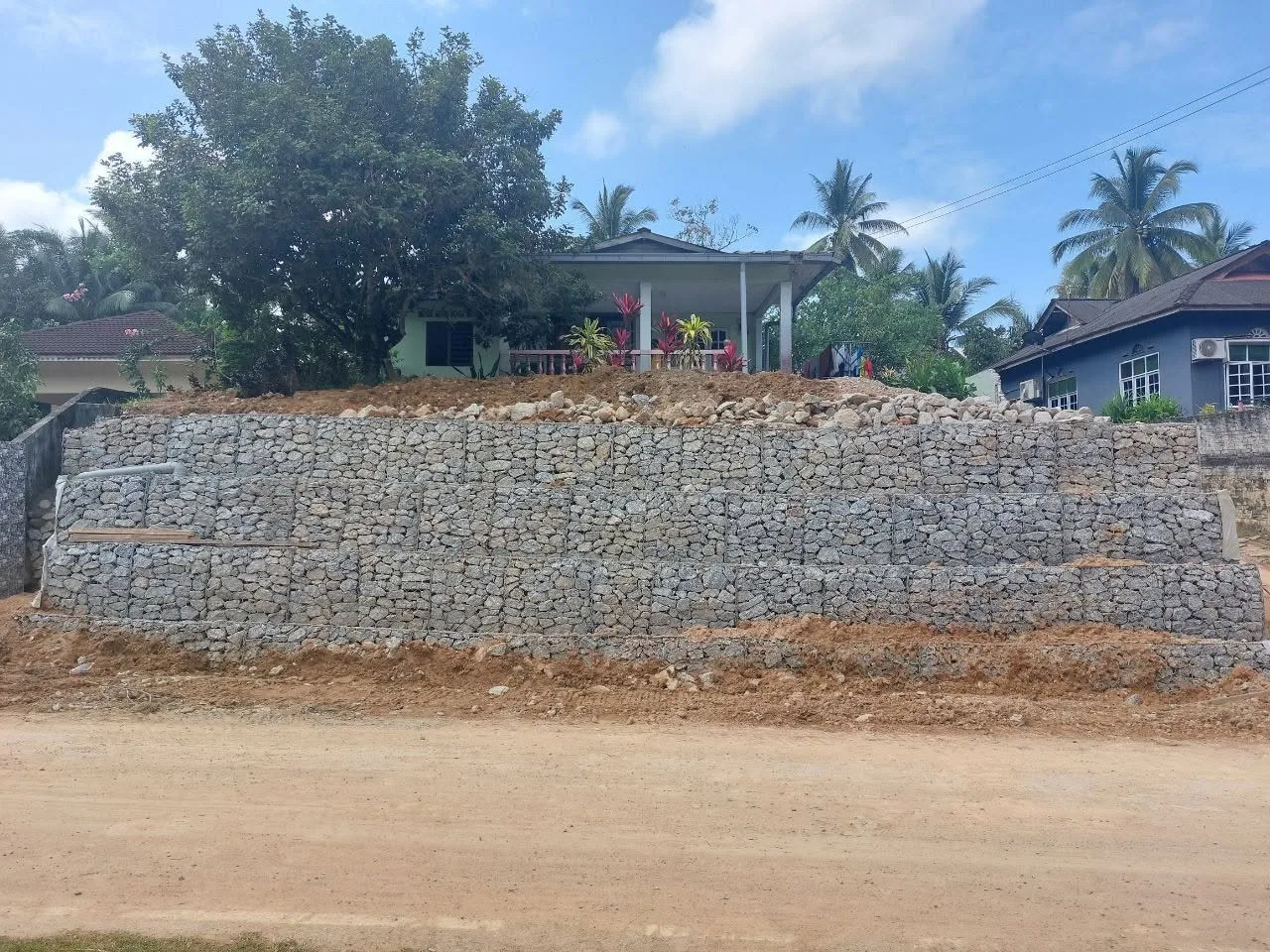 Tembok penahan gabion tiga lapis di tepi jalan kampung, menahan tanah kawasan rumah di aras lebih tinggi.